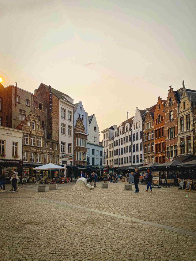 Una piazza cittadina acciottolata, circondata da tradizionali edifici a capanna e caffè all'aperto, durante un caldo tramonto.