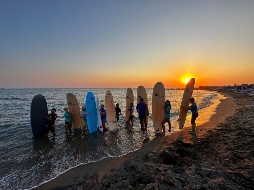 Un viaggio di gruppo WeRoad in posa con tavole da surf in mare su una spiaggia al tramonto.