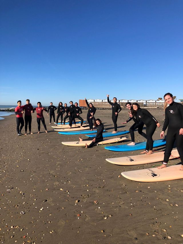 Un viaggio di gruppo WeRoad in mute da sub in posa con le tavole da surf su una spiaggia sabbiosa sotto un cielo sereno.
