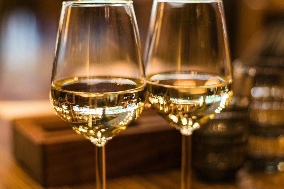 Un primo piano di due bicchieri di vino bianco, che riflettono le luci calde e soffuse della stanza.
