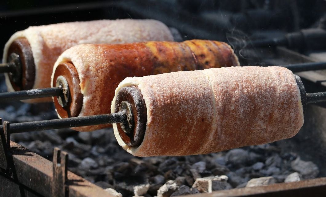 Trois gâteaux cheminée, des pâtisseries sucrées cylindriques, rôtissant sur des broches au-dessus de charbons ardents avec de la vapeur qui s'échappe.