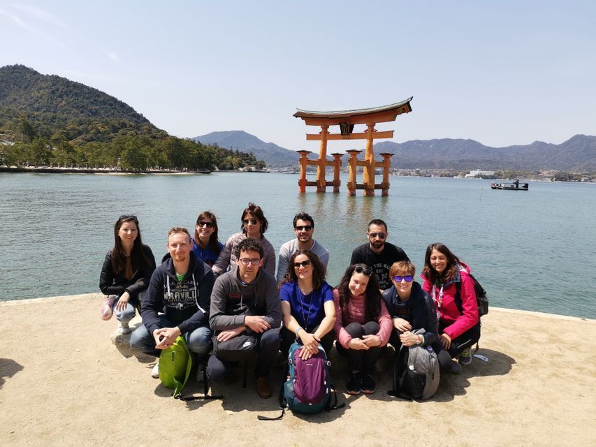 A WeRoad group trip posing for a photo on a shoreline in front of a large orange torii gate standing in the water.
