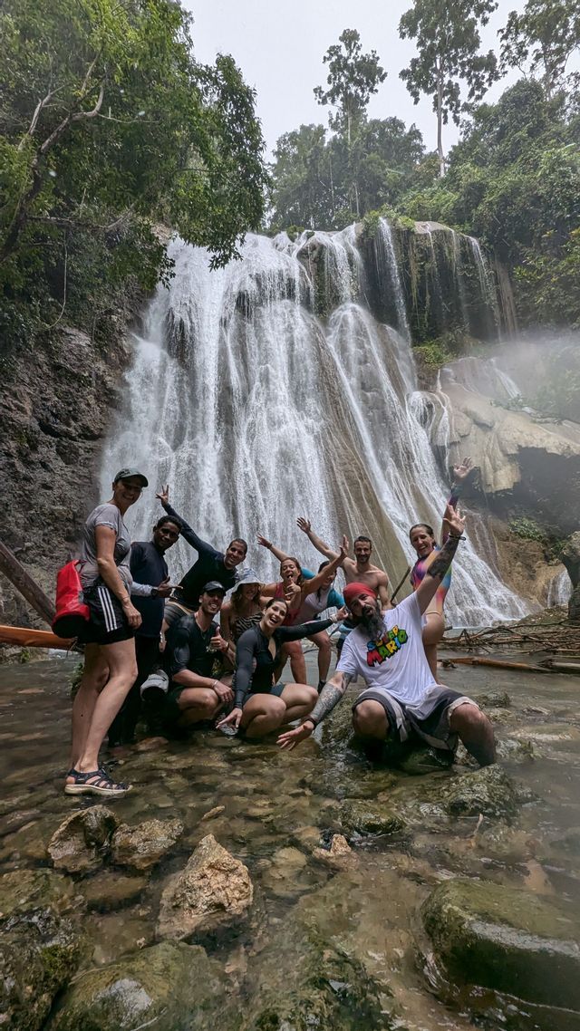 Un grupo de viaje de WeRoad sonríe y posa para una foto en el agua, en la base de una gran cascada.
