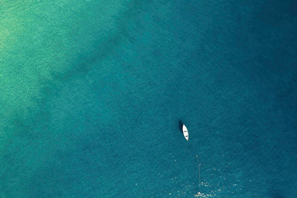 Una vista aerea di una piccola barca bianca che galleggia su una vasta distesa di acqua turchese.