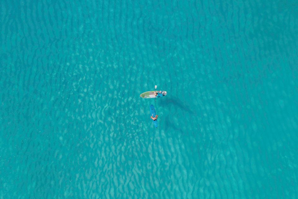 Una vista aerea di due persone di un viaggio di gruppo WeRoad che fanno paddleboard in acque calme e turchesi.