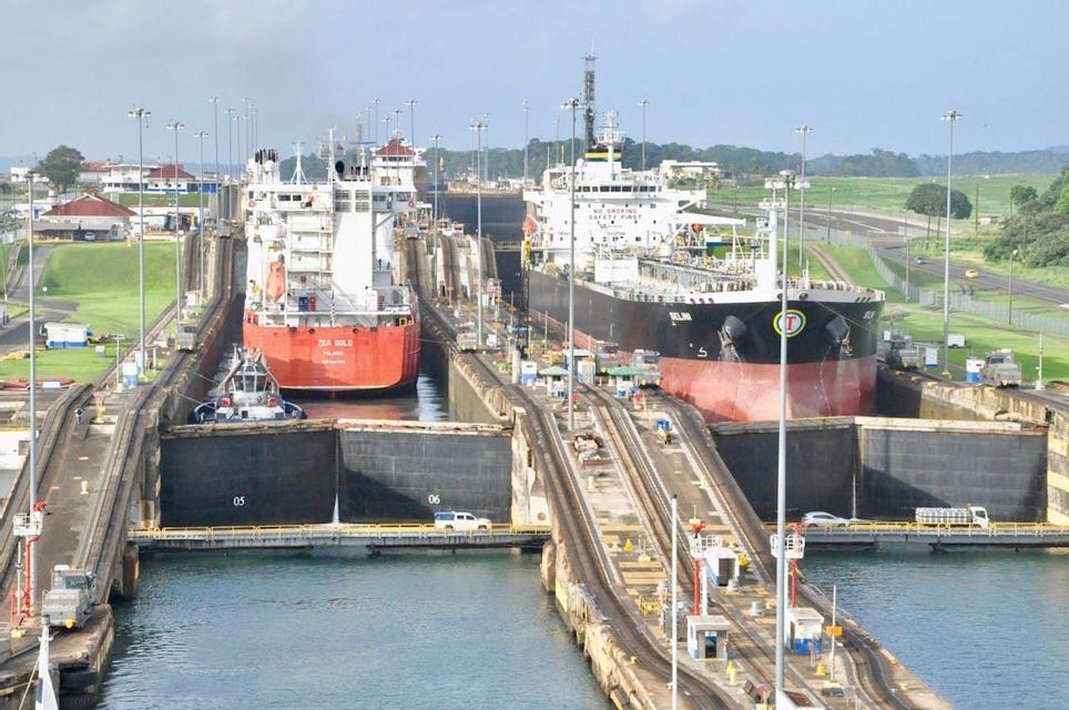 Due grandi navi cargo navigano attraverso un sistema parallelo di chiuse di canali in cemento circondate da un paesaggio verde.
