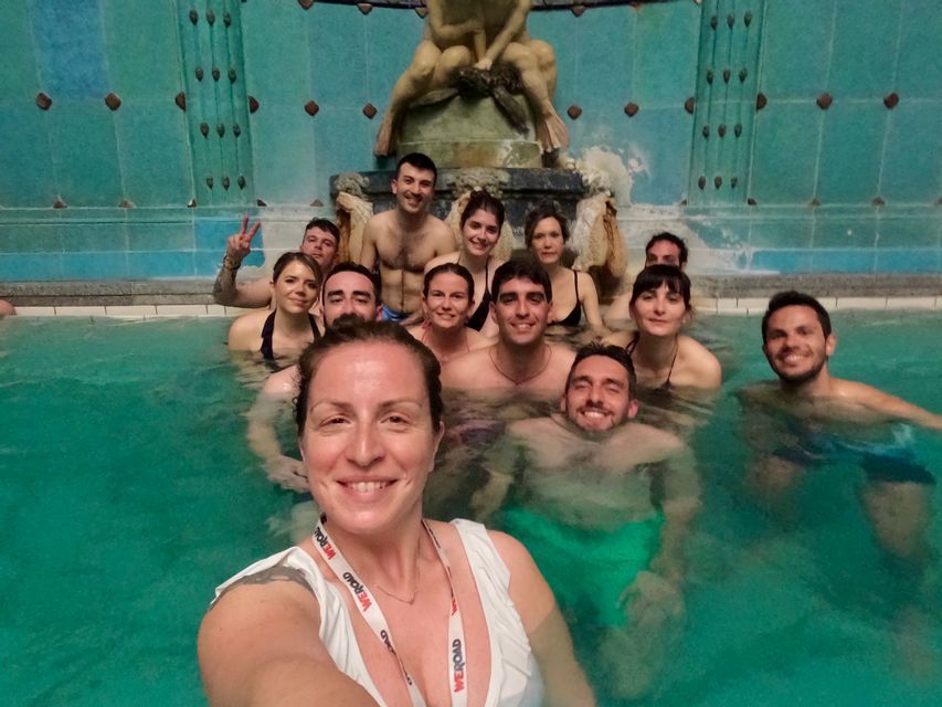Un gruppo WeRoad si fa un selfie mentre si rilassa in una piscina termale interna con una fontana decorativa.