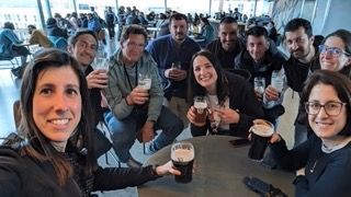 Un gruppo WeRoad sorride per un selfie mentre tiene in mano bicchieri di birra attorno a un tavolo al chiuso.