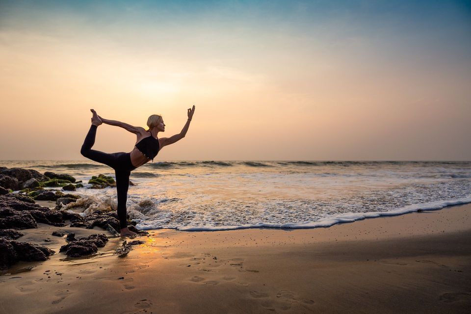 Una donna pratica una posa yoga in equilibrio su una spiaggia sabbiosa al tramonto.