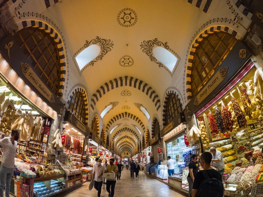 Una toma de ojo de pez de un mercado interior concurrido con techos abovedados decorados y puestos que venden especias y dulces.