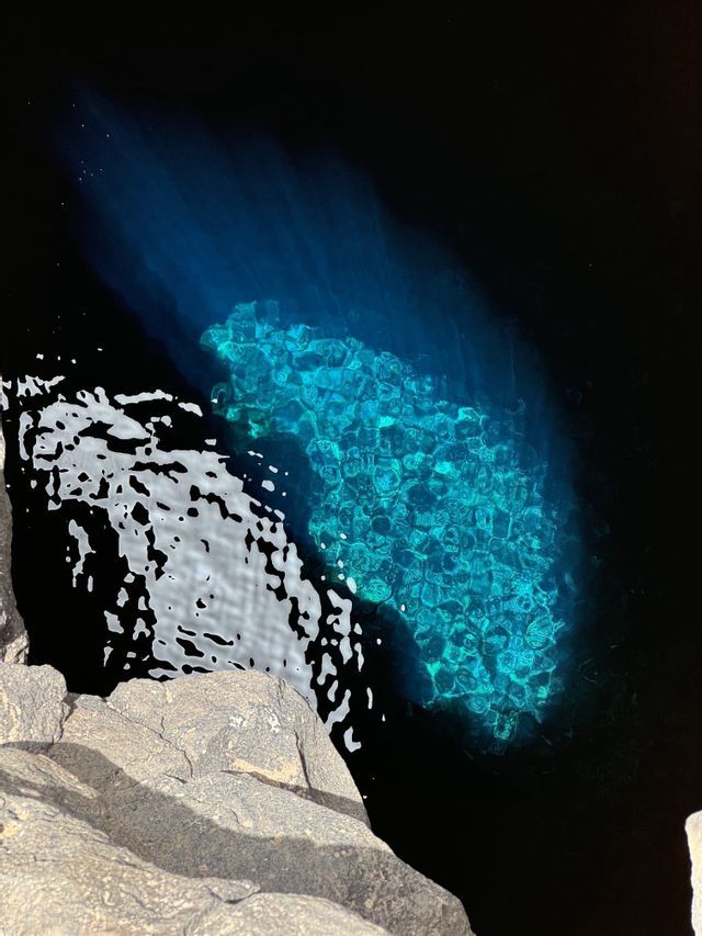 Un cuerpo de agua oscura con su fondo rocoso iluminado por una luz subacuática, creando un resplandor turquesa vibrante.