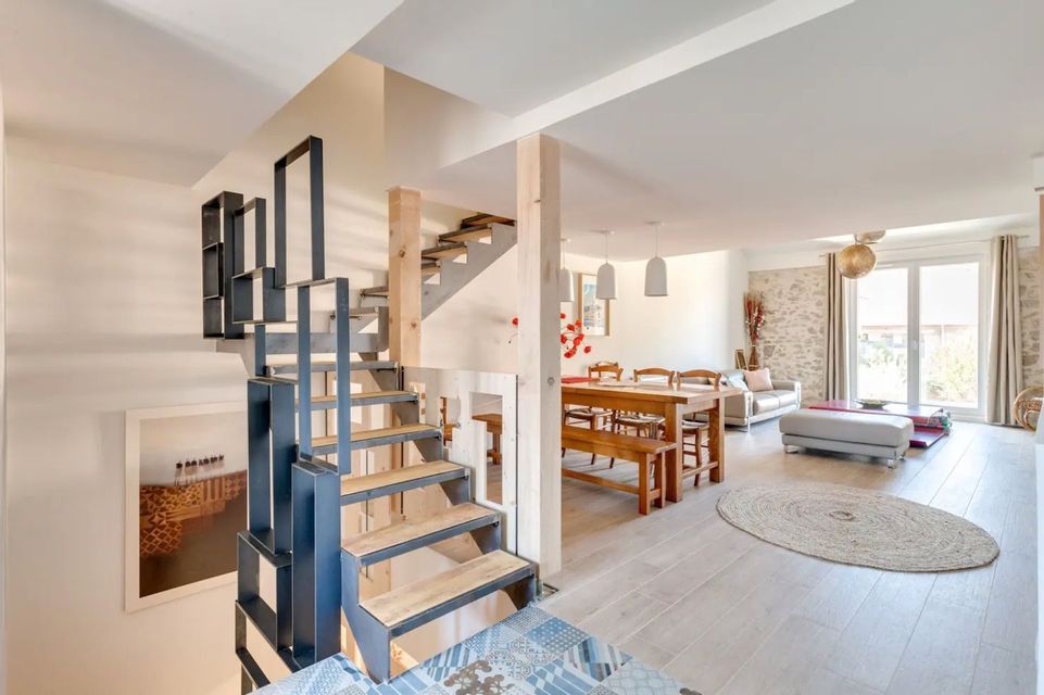 Un salon et une salle à manger modernes décloisonnés avec des parquets en bois clair, vus du haut d'un escalier en métal noir et bois.
