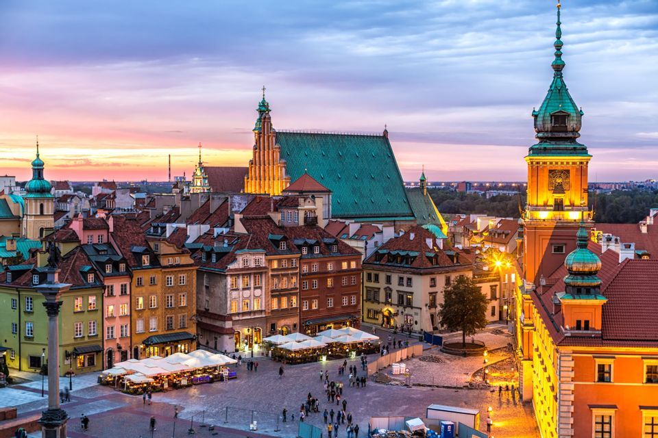 Una vista sopraelevata di una storica piazza europea al crepuscolo, con persone che passeggiano e cenano nei caffè all'aperto.