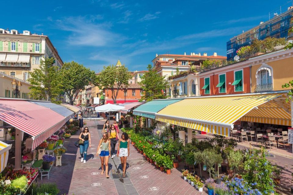 A WeRoad group trip of women walking through a sunny outdoor flower market with colorful striped awnings.