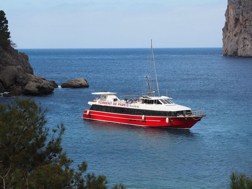 Eine WeRoad Gruppenreise auf dem Deck einer rot-weißen Fähre, die auf blauem Wasser nahe einer felsigen Küste segelt.