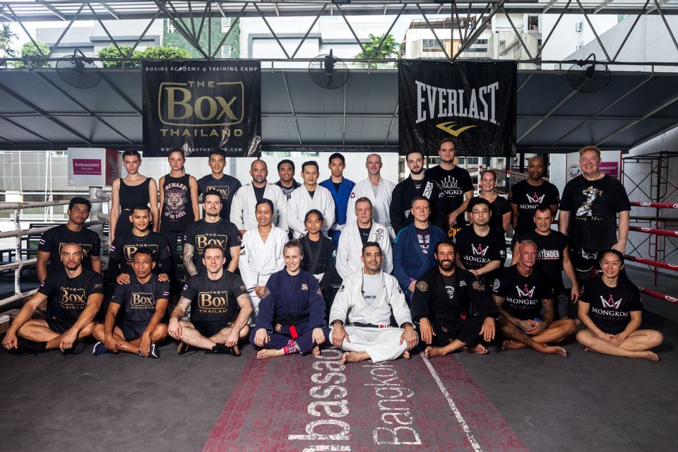 Un grand groupe de personnes en tenue de sport et kimonos d'arts martiaux posant pour une photo de groupe dans une salle de boxe.