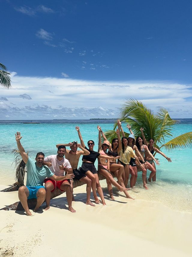 Un viaje en grupo de WeRoad posando juntos sobre un tronco de palmera en una playa de arena blanca junto a agua turquesa.