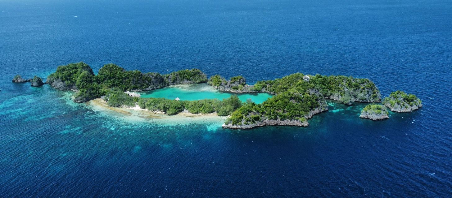 Vista aerea di piccole isole rocciose e verdi che formano un anello attorno a una laguna turchese in un oceano blu profondo