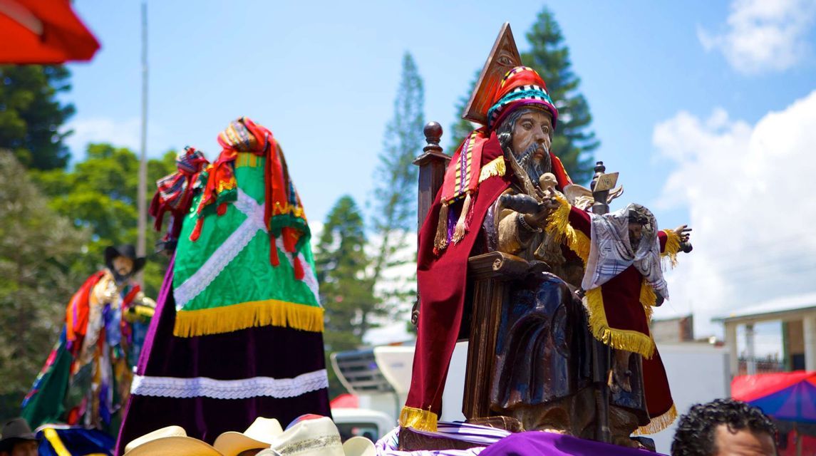 Close-up of two ornate statues in colorful robes being carried in an outdoor procession on a sunny day.