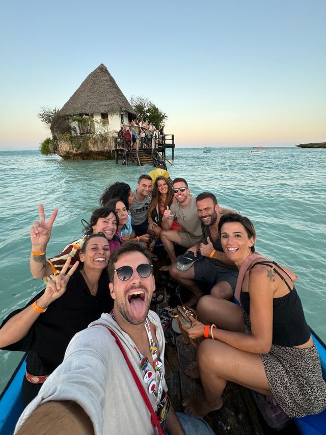 Un voyage de groupe WeRoad prend un selfie sur un bateau, avec un bâtiment sur un rocher en arrière-plan.