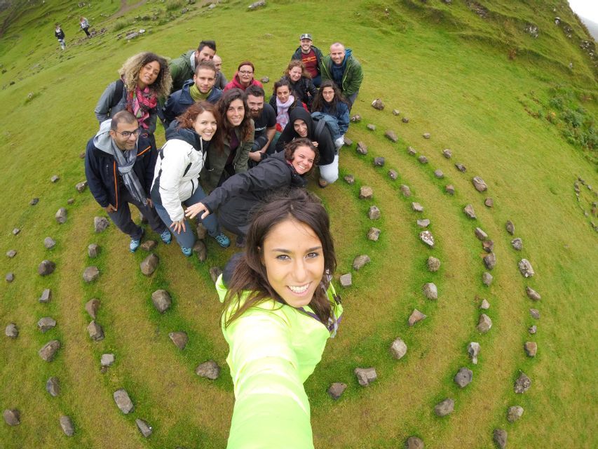 Un grupo de WeRoad se toma una selfie dentro de una formación espiral de piedra en una vibrante ladera verde.