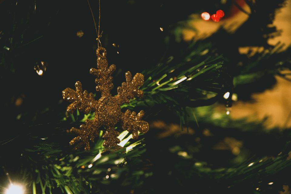 Un ornamento a fiocco di neve glitter oro pende tra i rami verdi di un albero di Natale con luci sfocate.