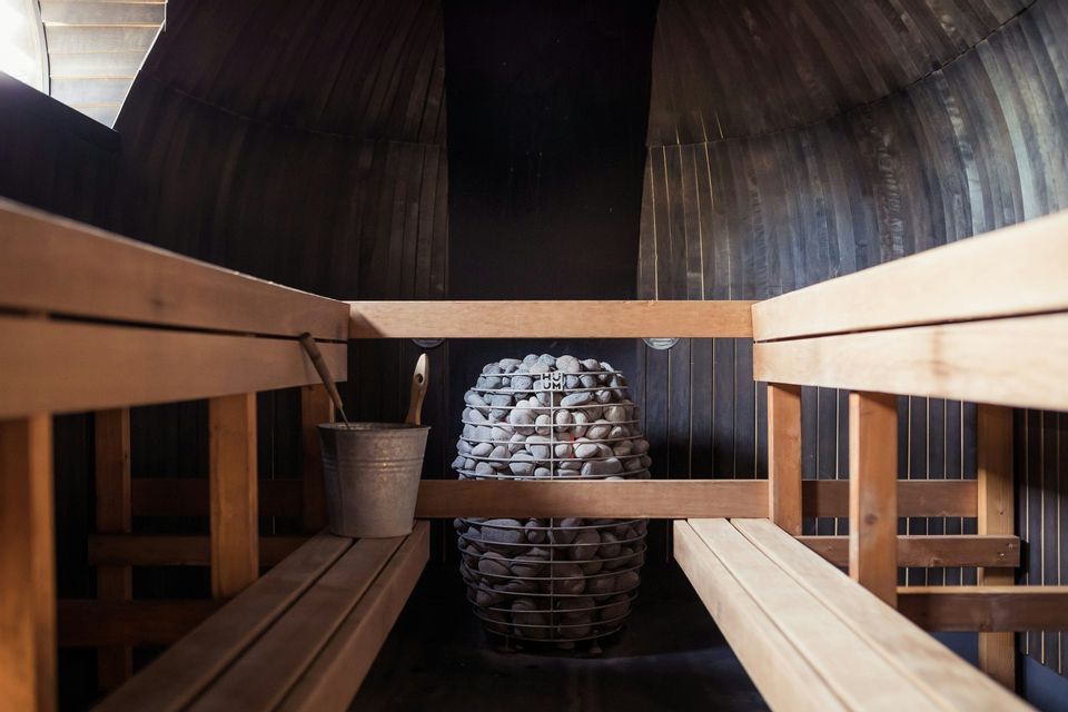 L'interno di una moderna sauna in legno con una stufa in pietra centrale, panche e un secchio.