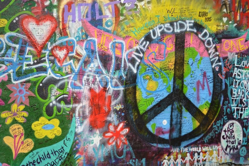 Un gros plan d'un mur coloré couvert de graffitis, présentant un grand signe de paix, des cœurs et divers messages écrits.