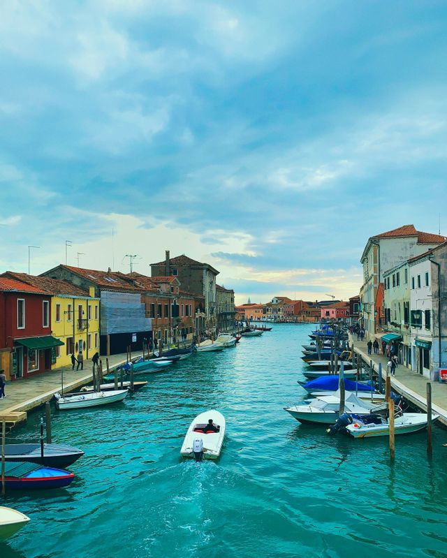 A high-angle view of a turquoise canal with a motorboat moving through it, flanked by colorful buildings and docked boats.