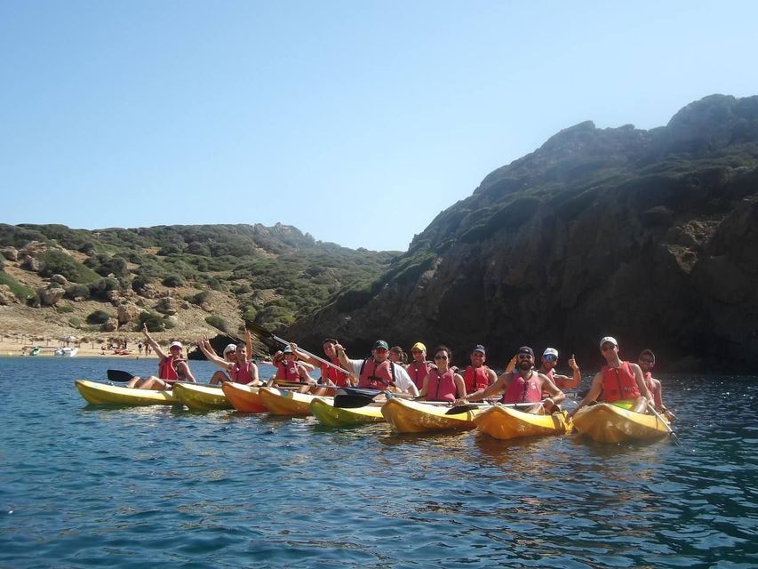 Un gruppo WeRoad in viaggio con giubbotti di salvataggio rossi è seduto in kayak gialli, in posa sul mare con una costa rocciosa alle spalle.