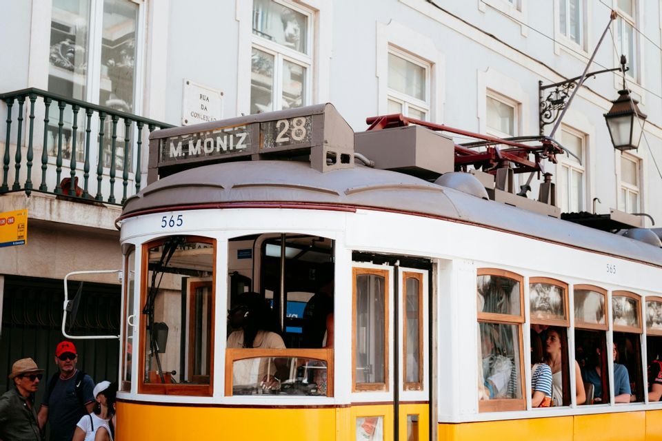 Un tram classico giallo e bianco numero 28 con passeggeri a bordo, fermo su una strada cittadina davanti a un edificio bianco.