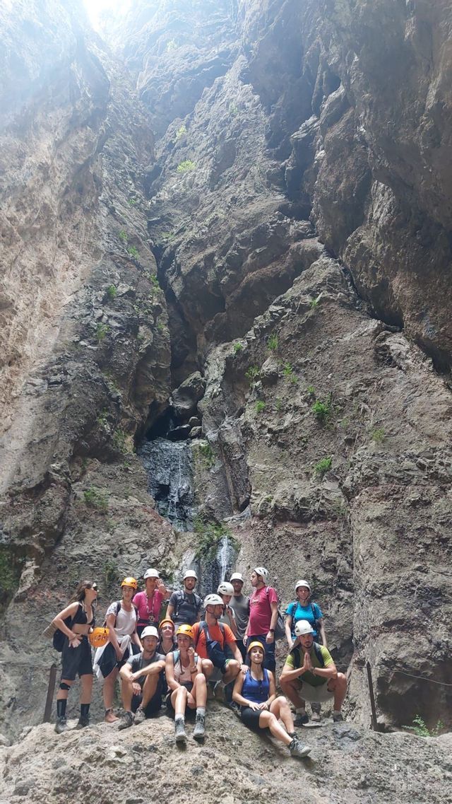 Un gruppo WeRoad in viaggio con i caschi posa per una foto su una roccia all'interno di un canyon profondo con una piccola cascata.