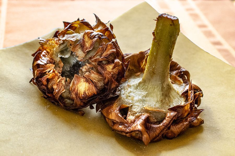 Un primo piano di due carciofi croccanti e fritti, adagiati su carta pergamena marrone su un tavolo.