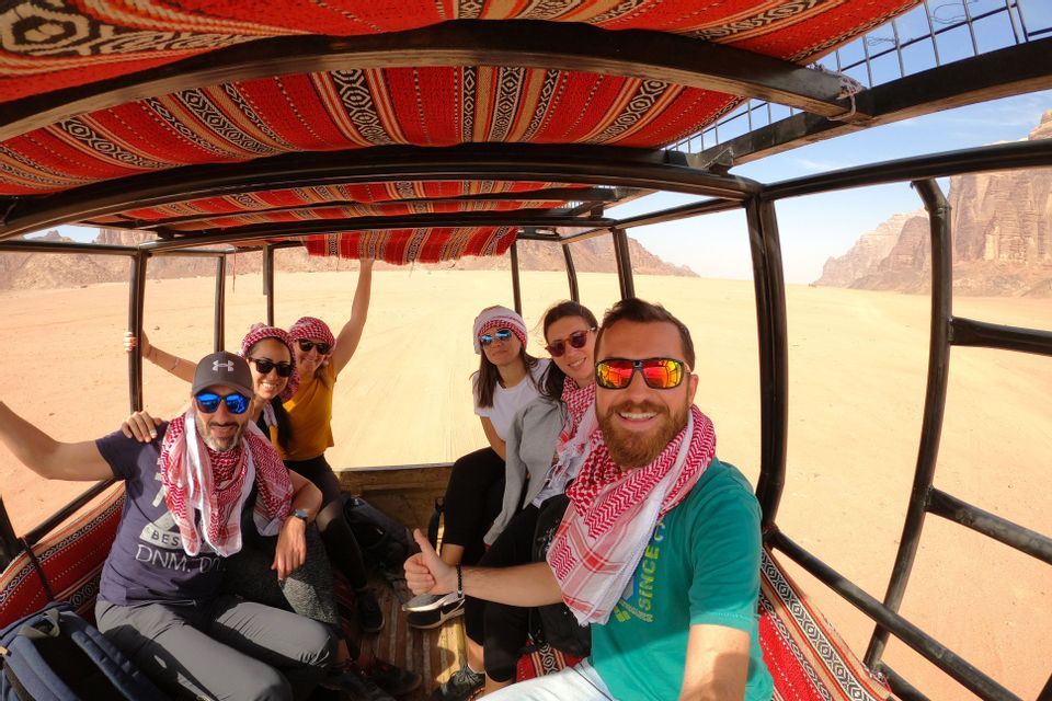 Un grupo de WeRoad se hace una selfie en la parte trasera de un vehículo abierto mientras conduce por un paisaje desértico.