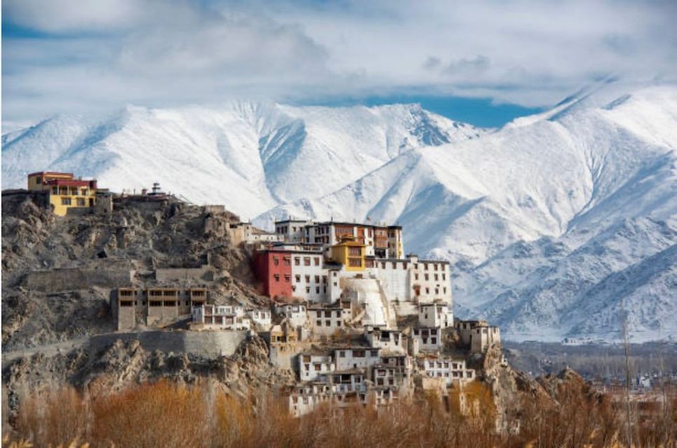 Un monastero colorato si erge su un fianco roccioso, con lo sfondo di imponenti montagne innevate.