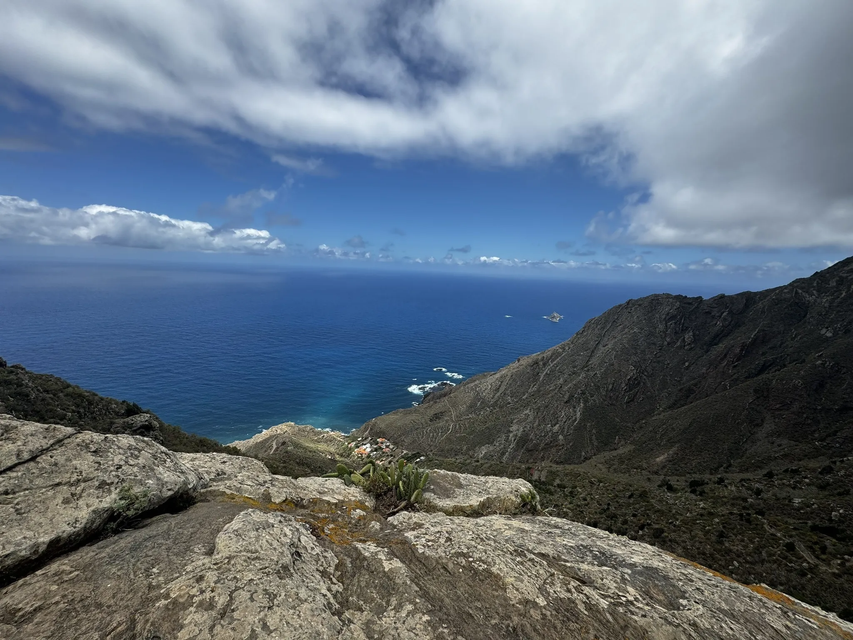 Vista da una scogliera rocciosa di una costa montuosa che si affaccia sull'oceano blu sotto un cielo parzialmente nuvoloso.