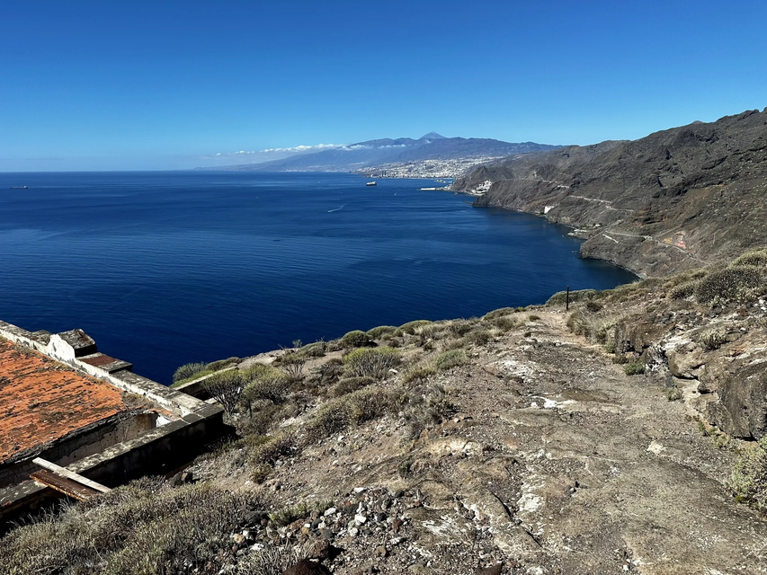 Una vista da una scogliera su un oceano blu intenso verso una costa vulcanica con una città e una montagna in lontananza.