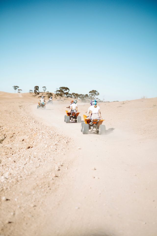 Un viaggio di gruppo WeRoad in quad in fila su una strada polverosa attraverso un paesaggio arido e collinare sotto un cielo azzurro.