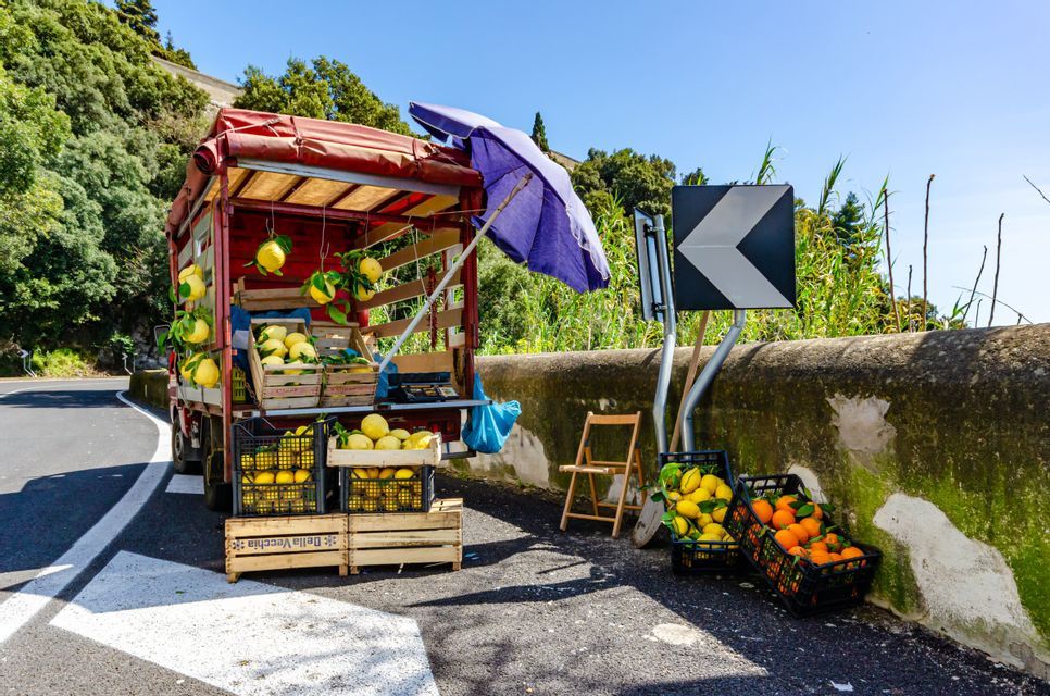Una bancarella di frutta a bordo strada sul retro di un camion rosso che vende casse di limoni e arance fresche in una giornata di sole.