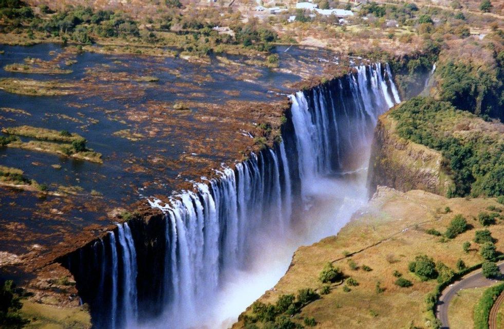 Veduta aerea di un'enorme cascata che precipita da un ampio fiume in una gola stretta, circondata da vegetazione secca e verde.