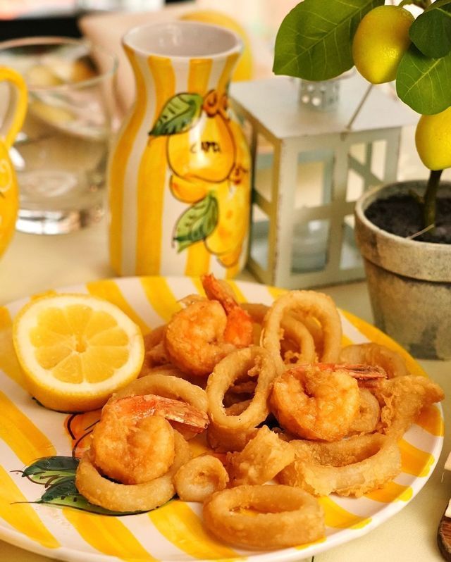 Un plato de calamares y camarones fritos con una rodaja de limón en un plato de rayas amarillas y blancas.