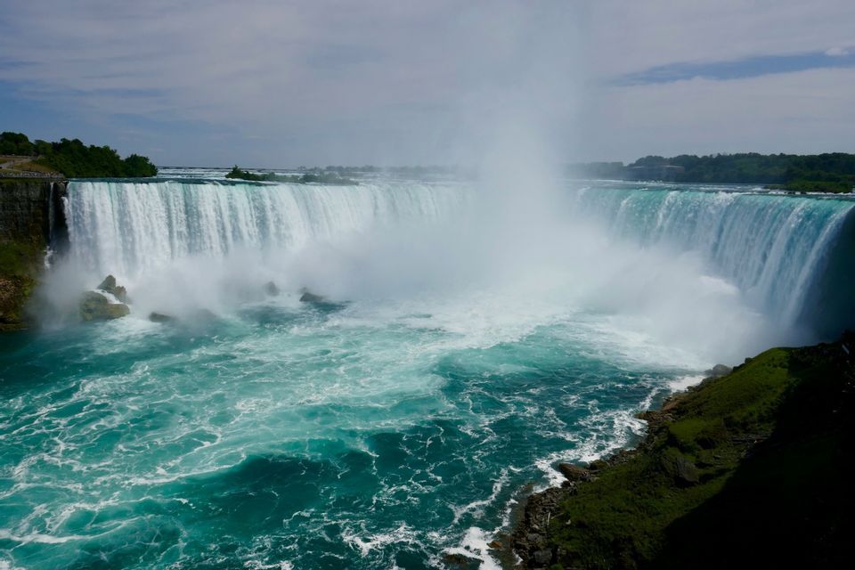 Un'ampia cascata a ferro di cavallo si getta in acque turchesi turbolente, sollevando una grande nuvola di nebbia.