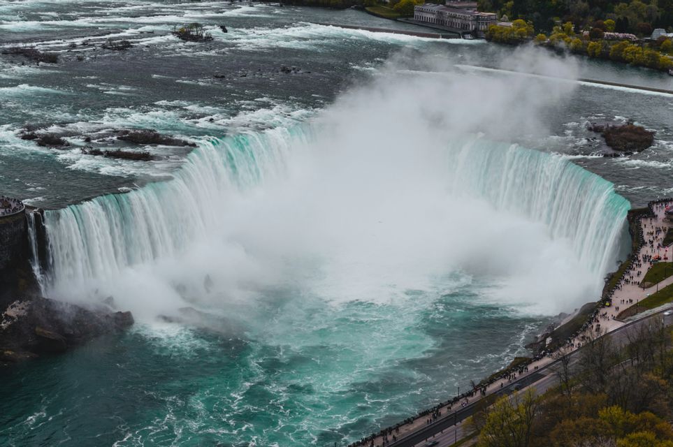 Una vista aerea di una potente cascata a ferro di cavallo, con una grande nuvola di nebbia che si solleva dall'acqua turbolenta sottostante.