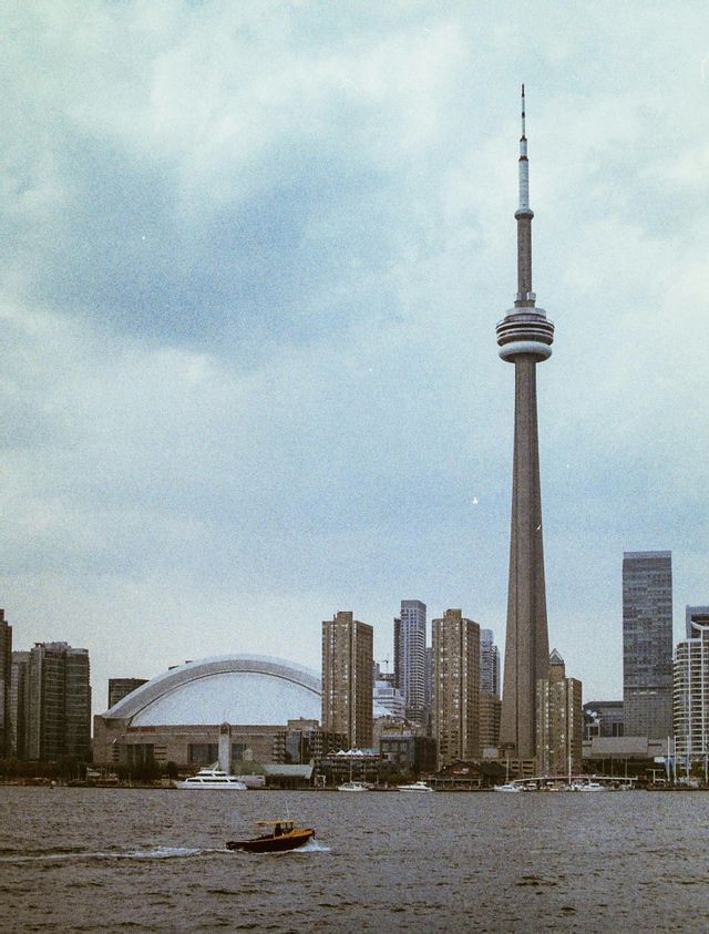 Una piccola barca a motore attraversa l'acqua davanti allo skyline di una città con un'alta torre di osservazione e uno stadio a cupola.
