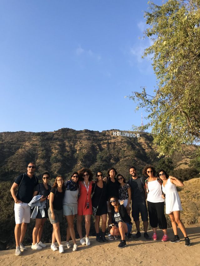 A WeRoad group trip poses for a photo on a hill with the Hollywood sign in the background on a sunny day.