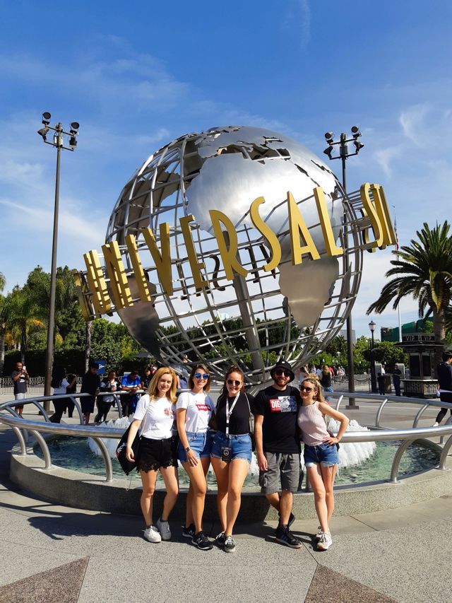 A WeRoad group trip of five people posing in front of the iconic Universal globe fountain under a clear blue sky.