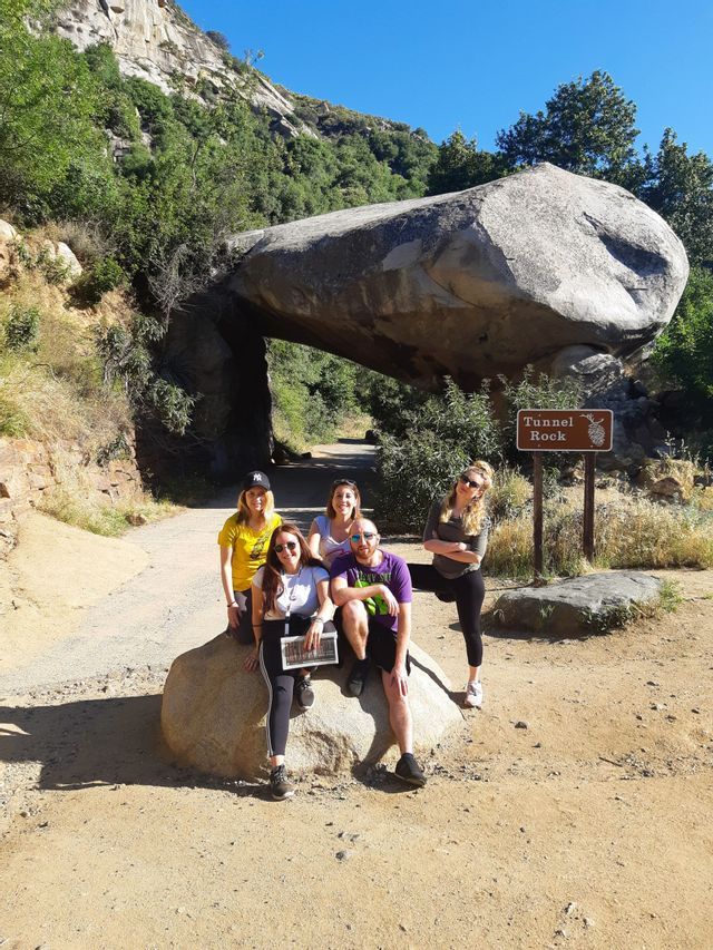 Un voyage de groupe WeRoad de cinq personnes posant pour une photo devant l'impressionnante formation rocheuse Tunnel Rock par une journée ensoleillée.