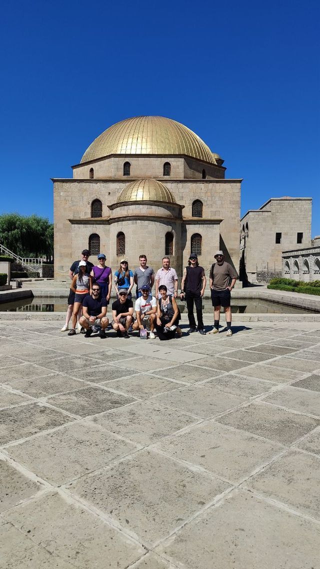 Un gruppo WeRoad in posa per una foto in un cortile di pietra, davanti a un edificio con una grande cupola dorata, sotto un cielo limpido e azzurro.