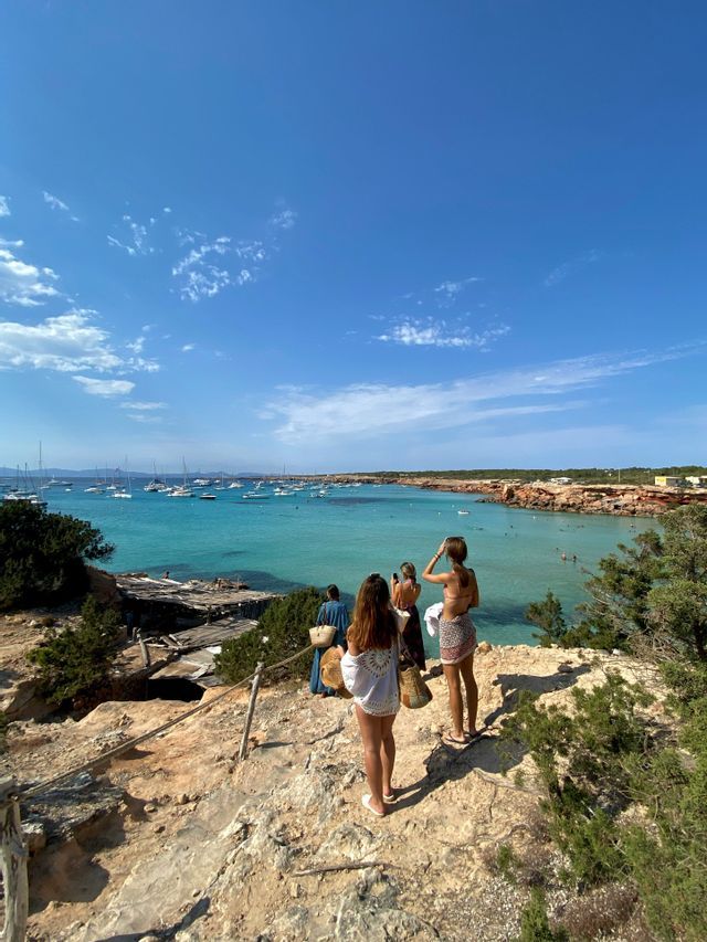 Un viaje en grupo WeRoad de mujeres en un acantilado rocoso con vistas a una bahía turquesa llena de veleros.