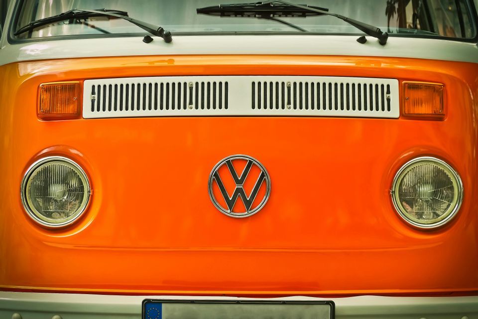 Primer plano del frontal de una furgoneta Volkswagen vintage naranja y blanca, mostrando su icónico logo y faros redondos.